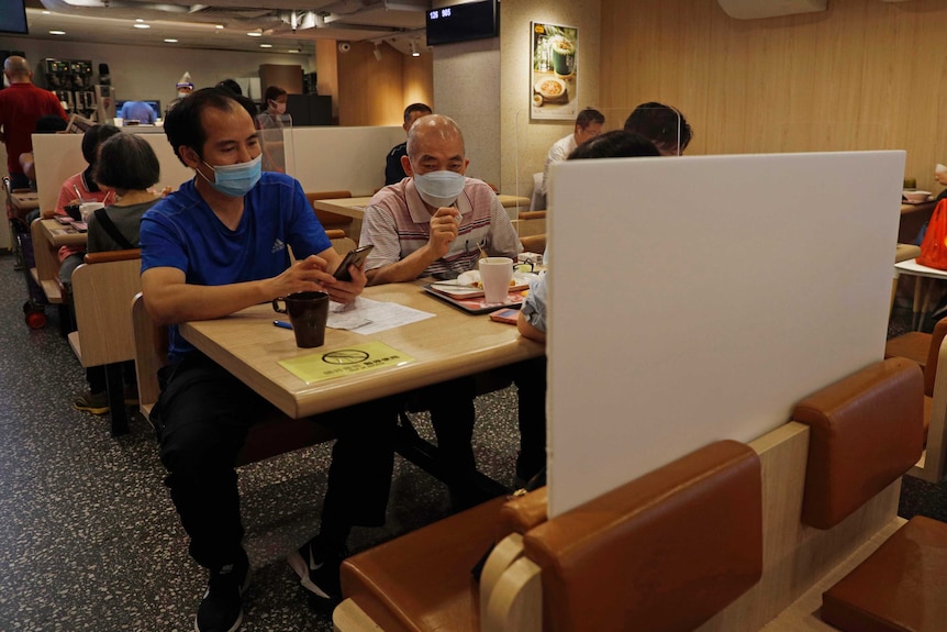 Two men wearing face masks are seated at a busy restaurant