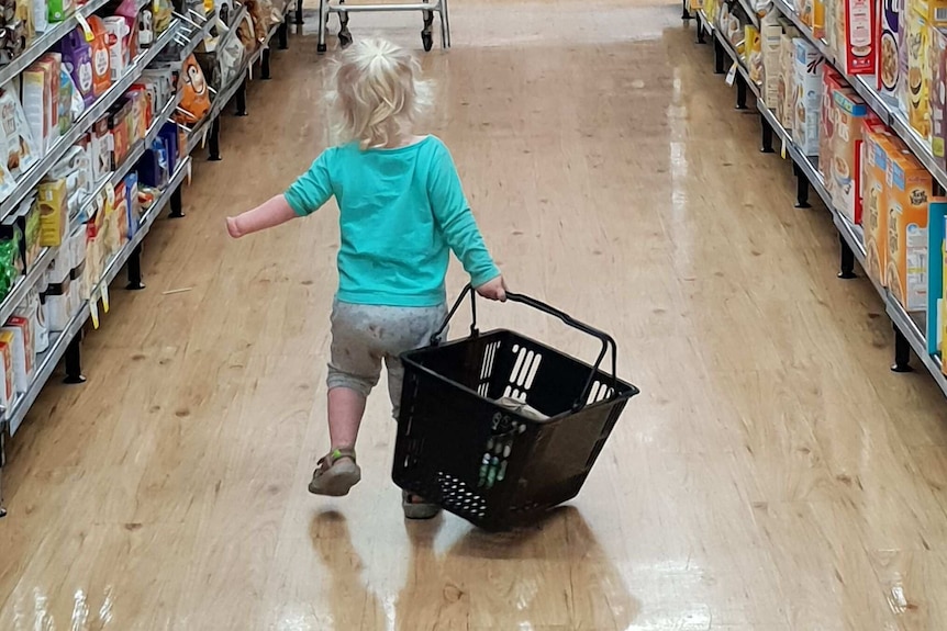 A picture of Izabella Carlson carrying a basket inside a supermarket, without a prosthetic hand.
