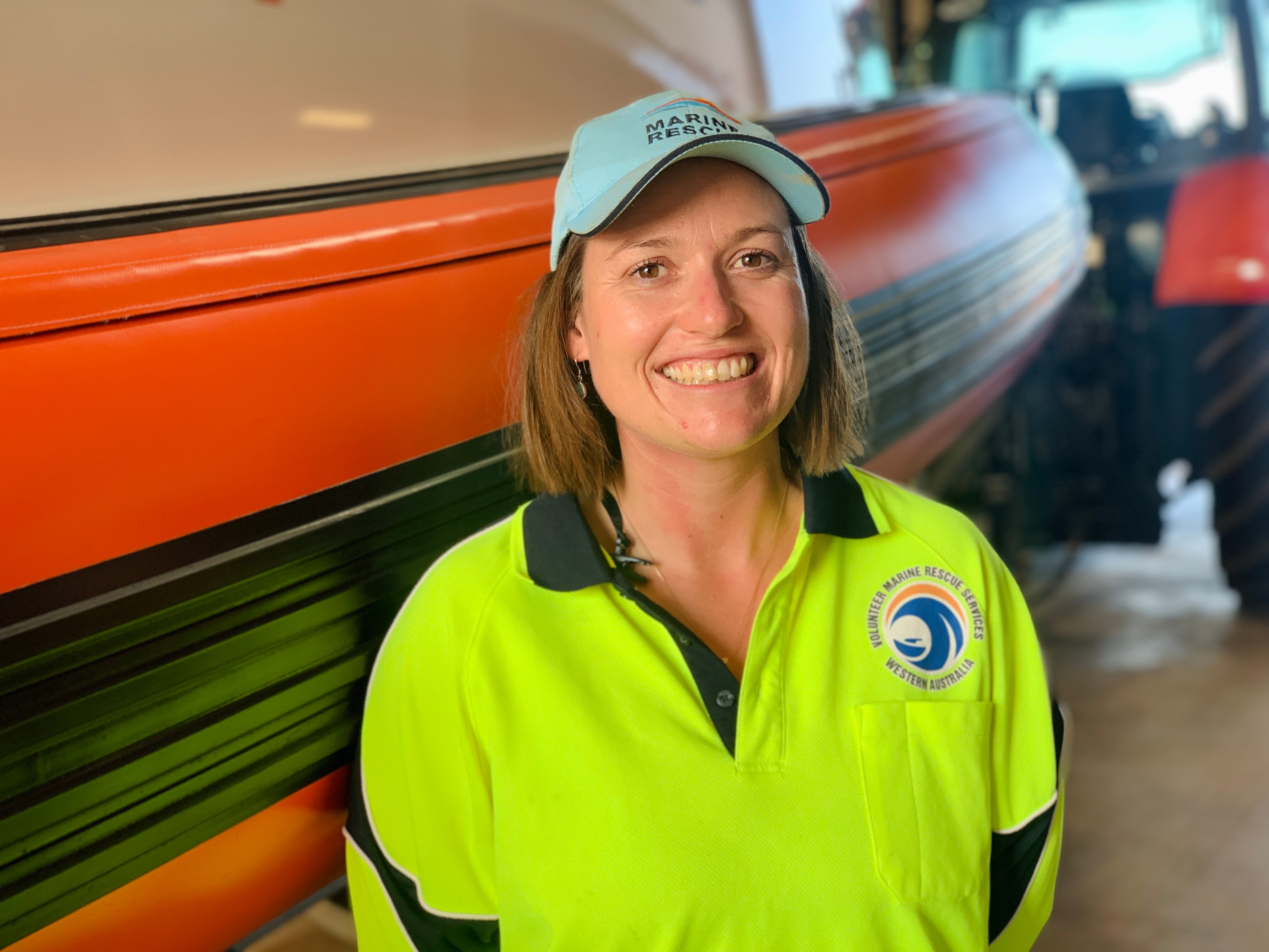 A woman in a fluro short stands smiling in front of a boat.