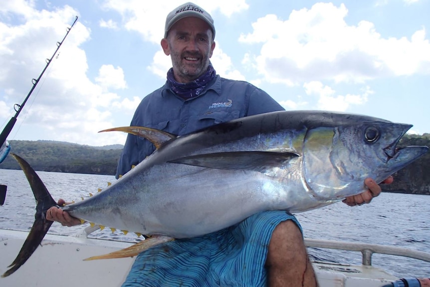 A man on a boat holding a large fish and smiling.