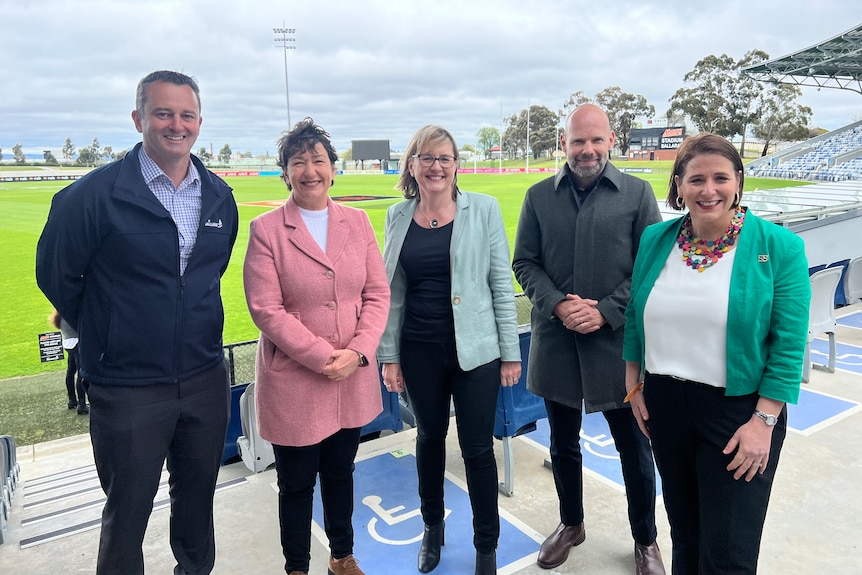 five politicians stand side by side smiling at ballarat's eureka stadium