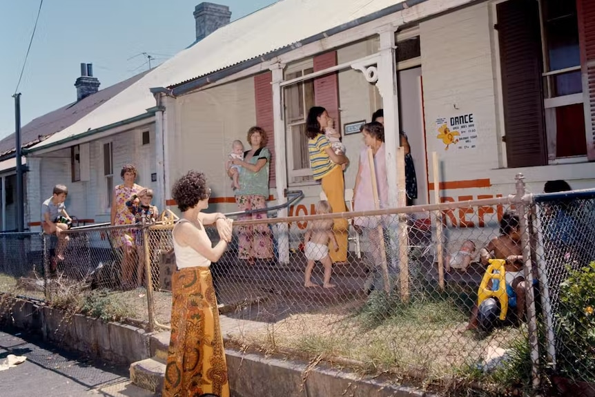 Kids and mothers outside a terrace house with toys in the yard