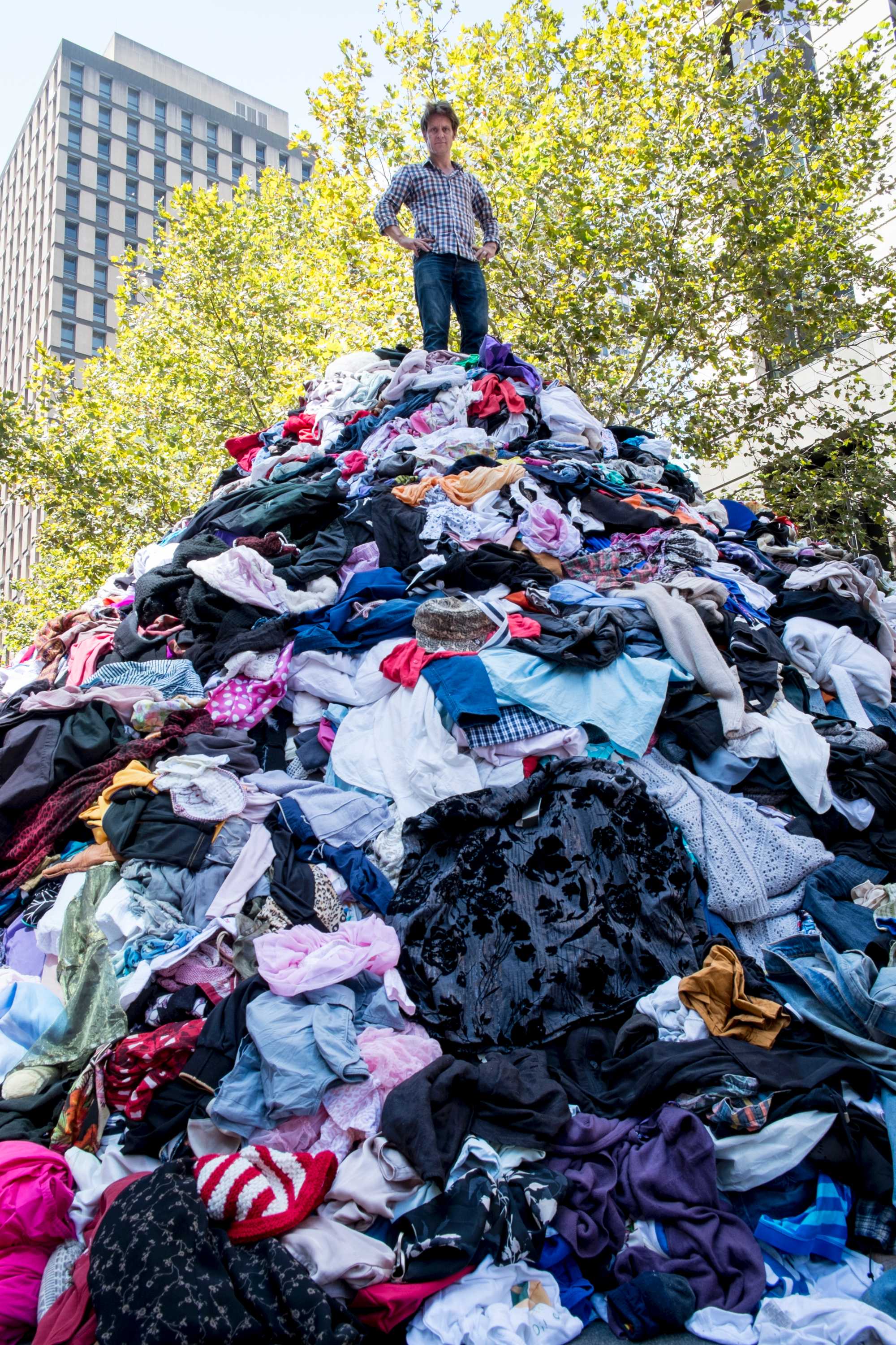Craig Reucassel standing on top of a mountain of clothes in Martin Place to illustrate the problem of 'fast fashion'.
