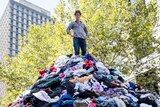 Craig Reucassel standing on top of a mountain of clothes in Martin Place to illustrate the problem of 'fast fashion'.
