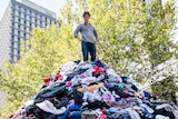 Craig Reucassel standing on top of a mountain of clothes in Martin Place to illustrate the problem of 'fast fashion'.