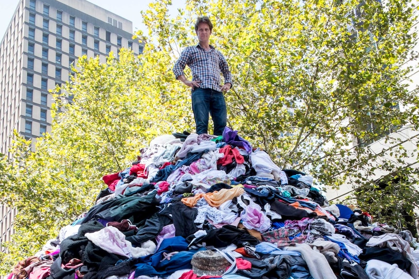 Craig Reucassel standing on top of a mountain of clothes in Martin Place to illustrate the problem of 'fast fashion'.