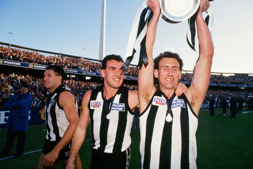 Peter Daicos holds up the Premiership Cup while Darren Millane smils in the background.