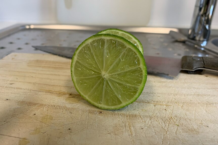 A sliced lime on a chopping board with knife.