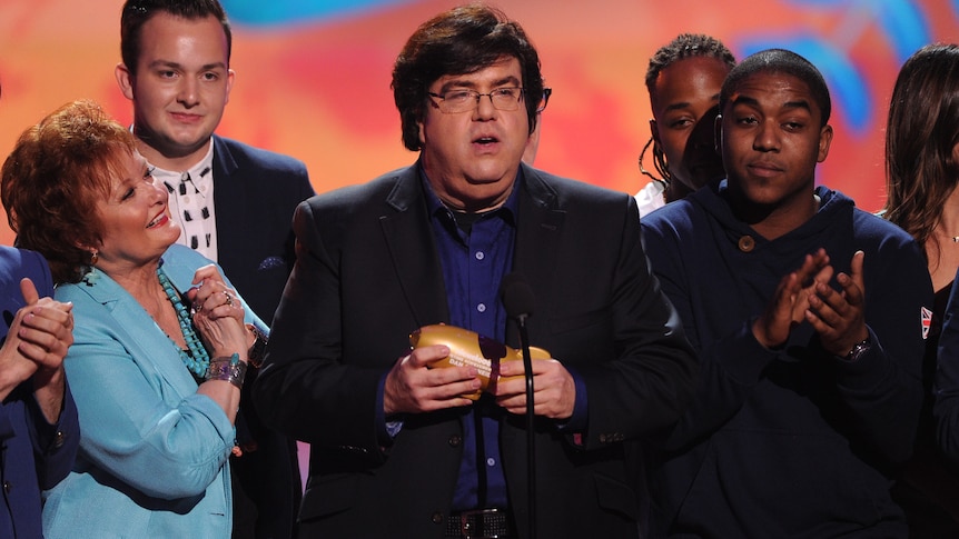 Nickelodeon producer Dan Schneider on stage with an award surrounded by people