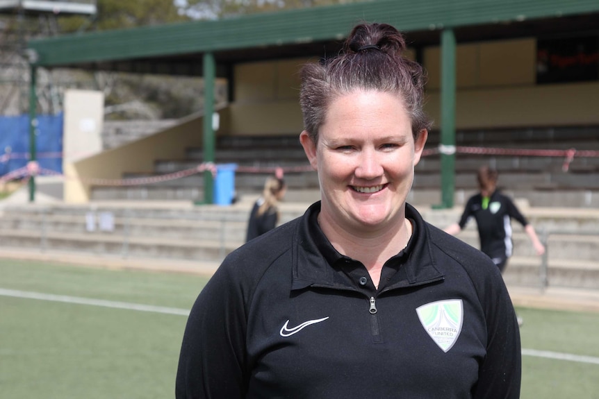 Una mujer en un campo deportivo sonríe a la cámara.