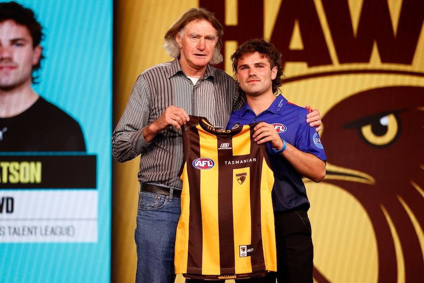Nick Watson and Michael Tuck stand together on stage and hold a Hawthorn jersey