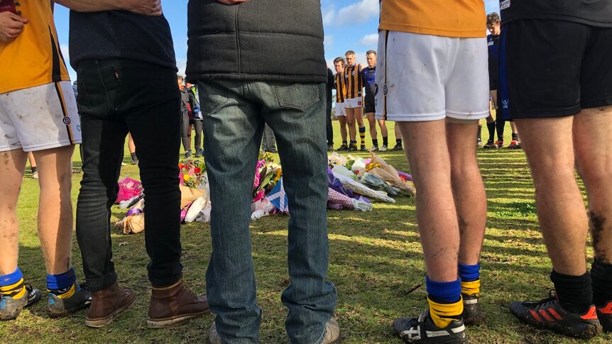 Footy players link arms and formed a circle around a memorial of flowers for Eurydice Nixon.