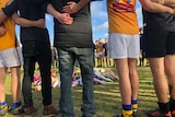 Footy players link arms and formed a circle around a memorial of flowers for Eurydice Nixon.