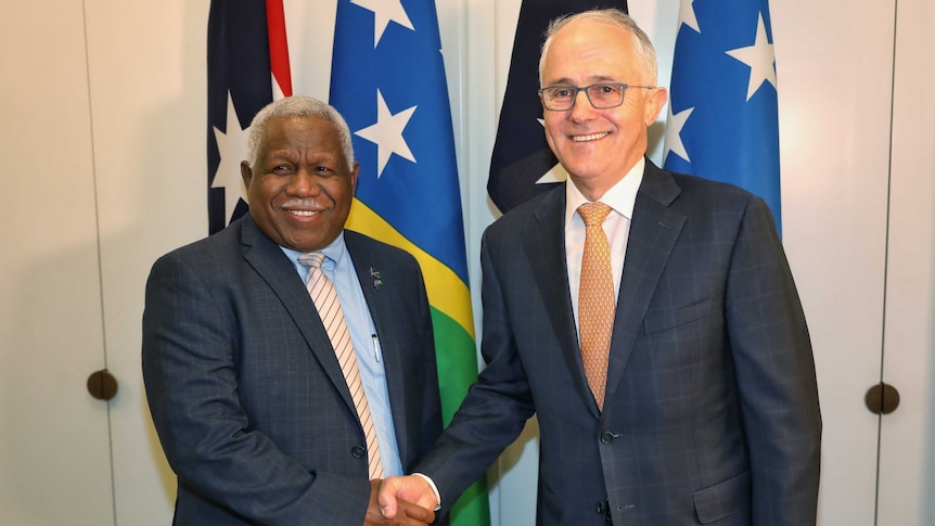 Malcolm Turnbull and Rick Houenipwela stand side by side, smiling while shaking hands.