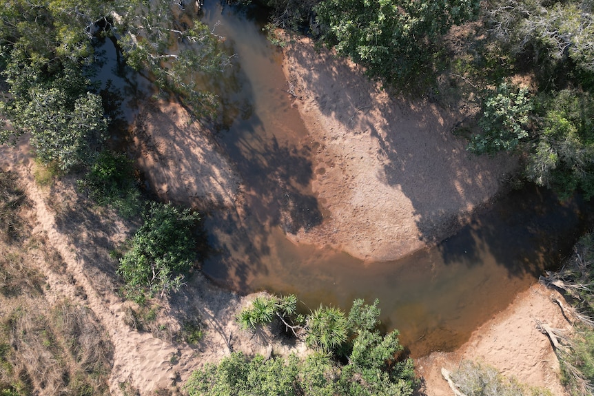 An aerial image of a brown river surrounded by sandy banks and green trees