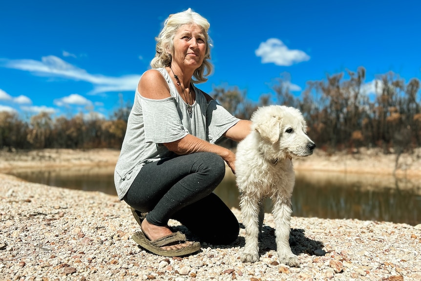 a woman bends down to pat a white puppy near a dam
