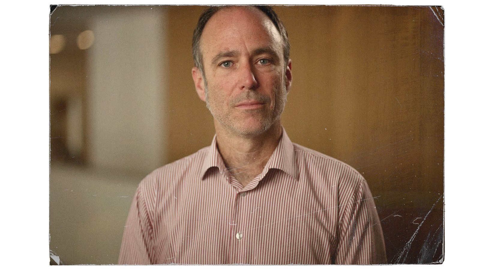 A man wearing a red checked shirt stares seriously towards the camera