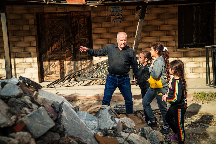 A man dressed in a black shirt and jeans directs children around a pike of rubble on the road