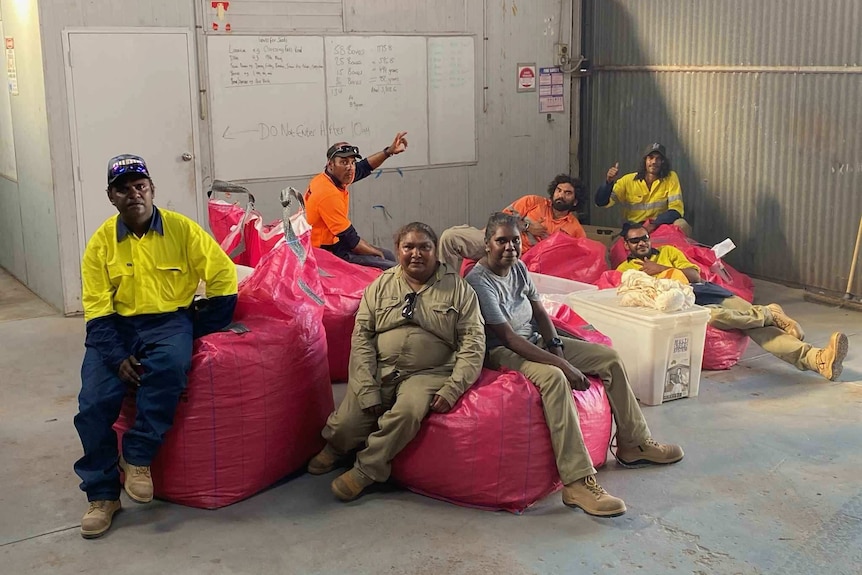 A group of East Kimberley residents sit on bags of collected seed inside warehouse