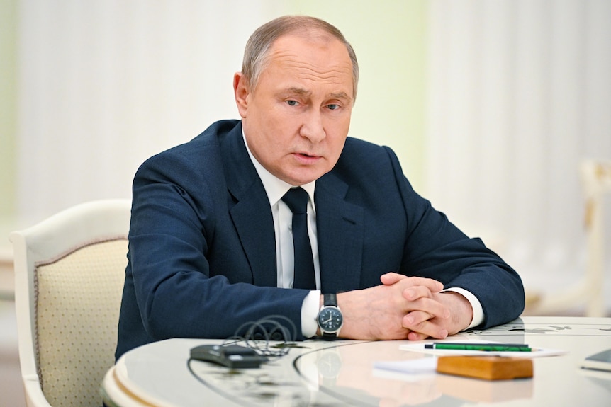 Middle aged man in navy suit seated at white table.