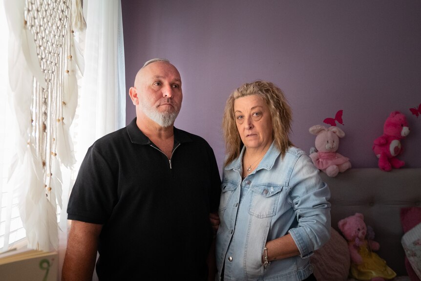 A couple stand in a child's bedroom, looking serious.