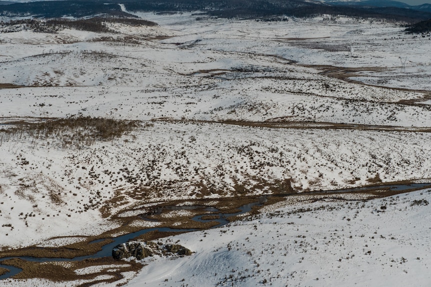 A landscape photo of a river surrounded by snow with mountains surrounding it.