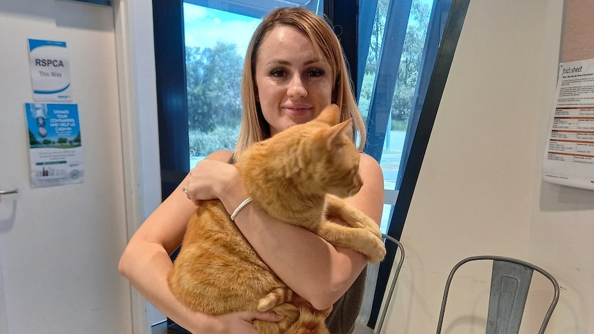 A young smiling woman holds a large ginger cat.