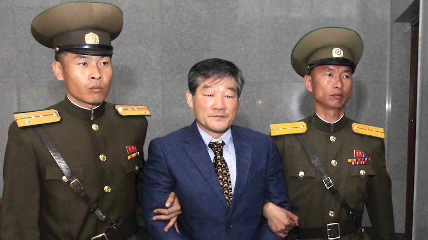 Kim Dong Chul stands between two North Korean guards with handcuffs on.