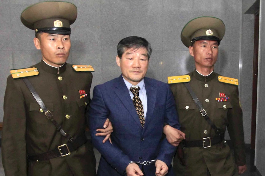 Kim Dong Chul stands between two North Korean guards with handcuffs on.