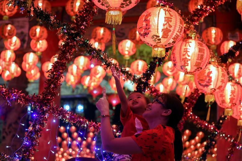A mother holds up her daughter, as they spend time under lanterns and decorations to celebrate during the Chinese Lunar New Year