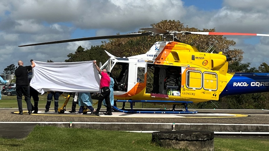 Paramedics help a man from a medical helicopter, hidden behind a sheet