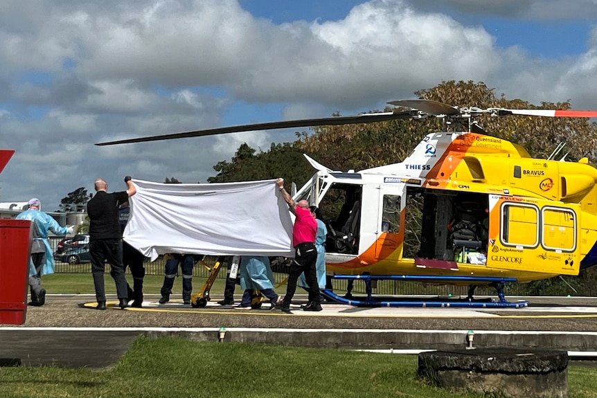 Paramedics help a man from a medical helicopter, hidden behind a sheet