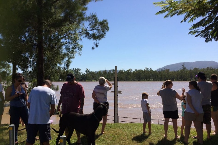 Residents stand near a flood level indicator as waters rise in Rockhampton