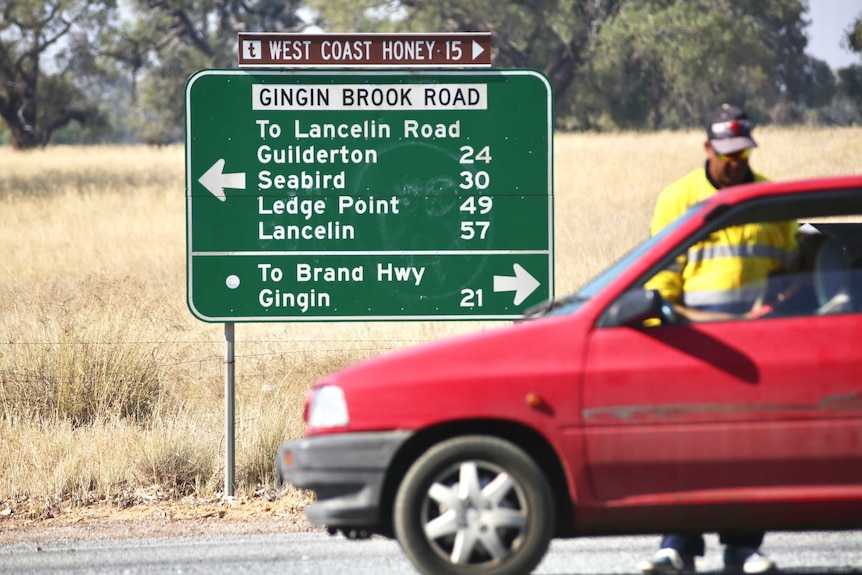 A directional sign on a country road with a car blocking traffic