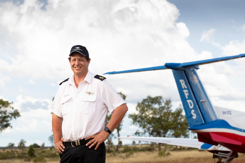 A Royal Flying Doctor stands in front of a plane with a big smile in outback Queensland