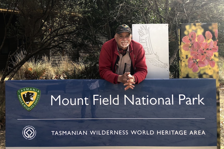 Darroch is an older man with white hair and white beard. He is leaning over a sign that says Mount Field National Park.
