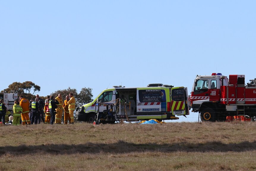 Wide image of an open field with emergency services vehicles standing around.