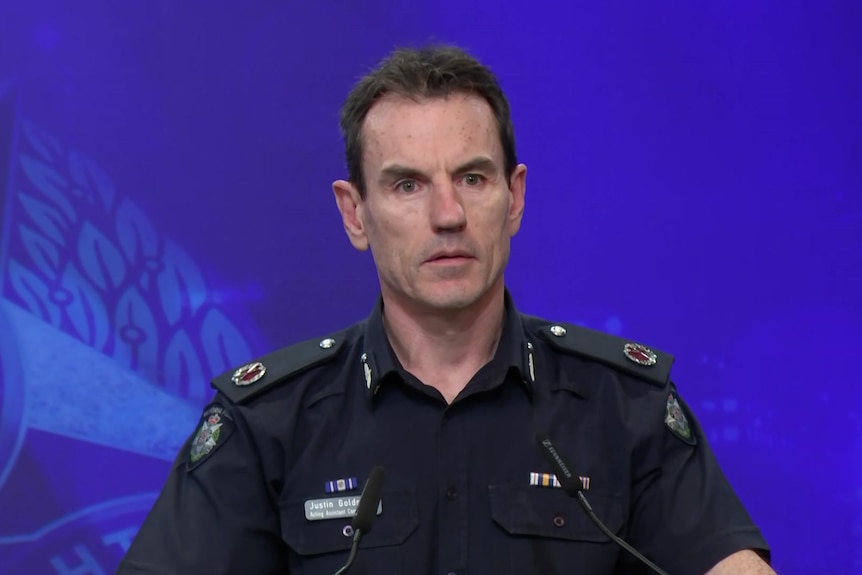 A police officer in uniform addresses media at a lectern.