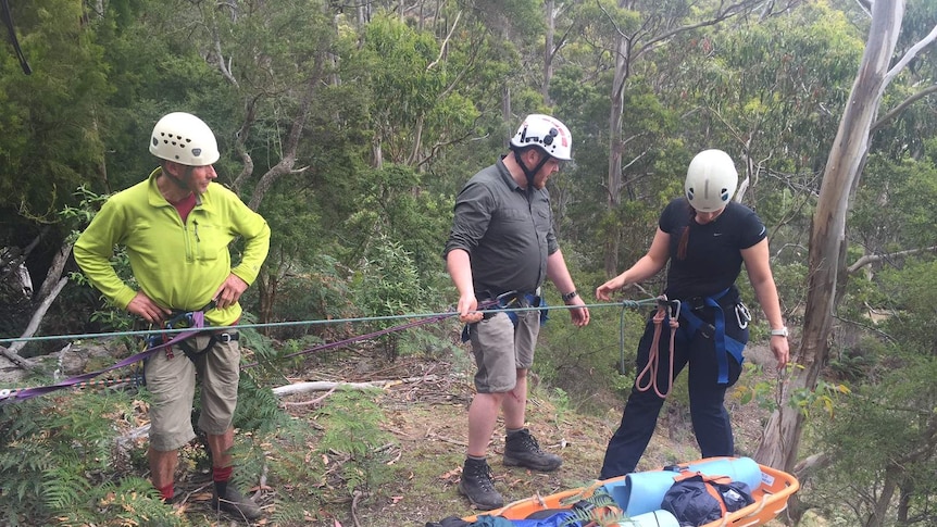 A team prepares to lower a rescuer down a cliff.