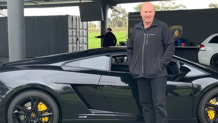 a man stands in front of a sports car