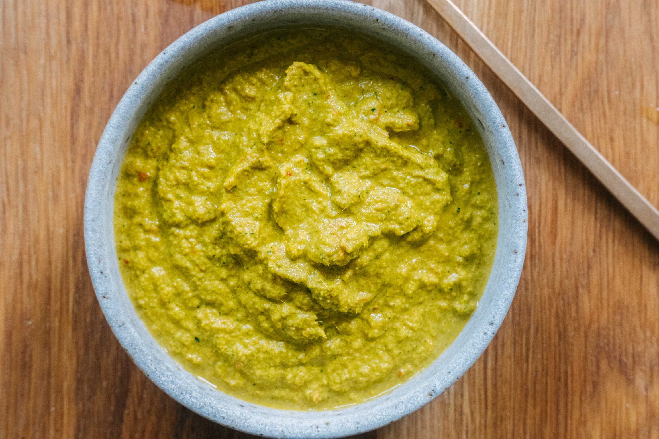 A white bowl full of vibrant yellow curry paste on a wooden table.