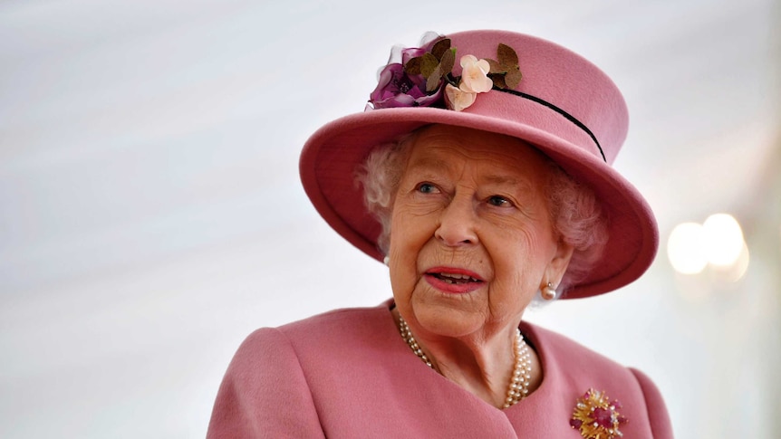 Queen Elizabeth wears a rose pink hat with flowers on it and a matching coat during a visit to Porton Down.