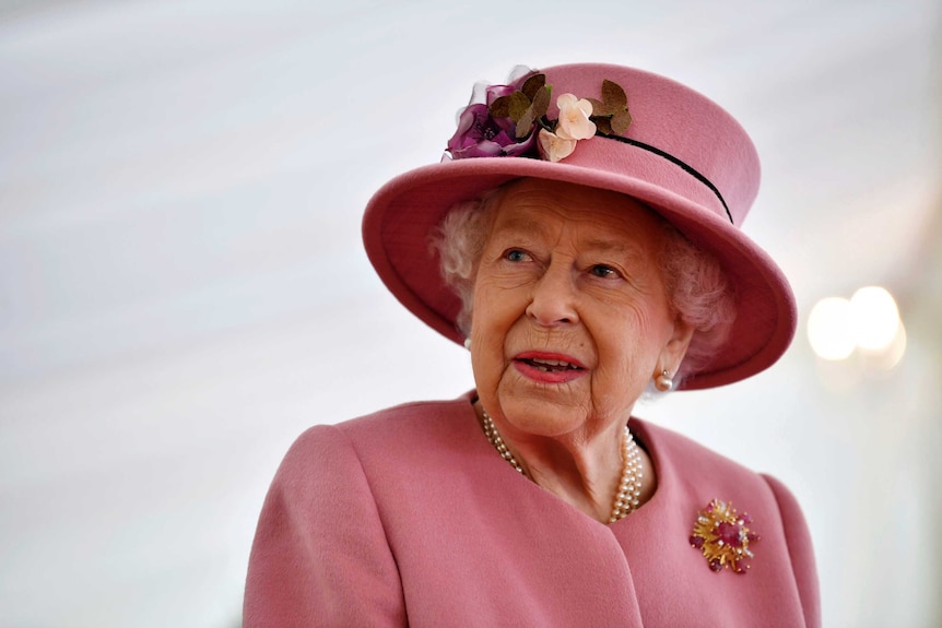 Queen Elizabeth wears a rose pink hat with flowers on it and a matching coat during a visit to Porton Down.