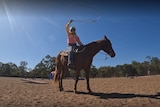 A woman sits on horseback and swings a lasso above her head.