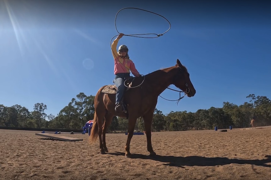 A woman sits on horseback and swings a lassoo abover her head