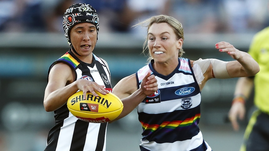 A Collingwood AFLW player attempts to kick the ball while under defensive pressure from a Geelong opponent.