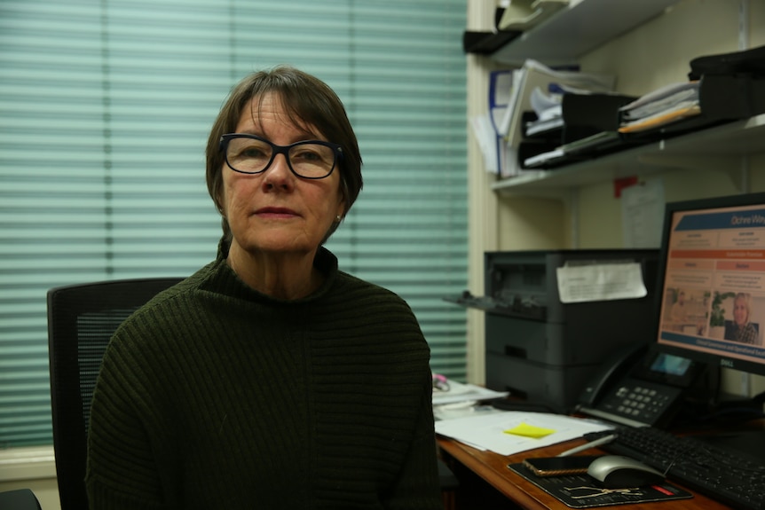 A dark-haired, bespectacled doctor sits in her office.