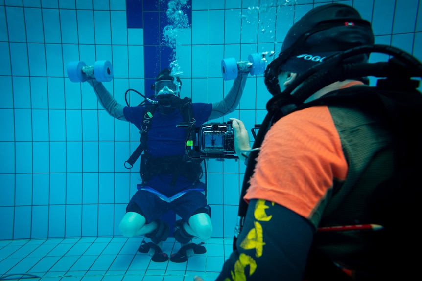 A man wearing a scuba suit lifting weights underwater 