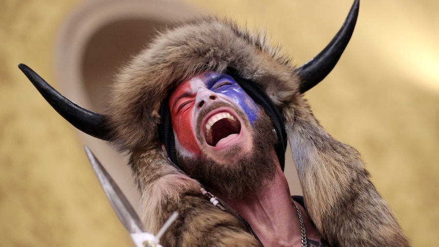 A man wearing a horned fur hat holding a spear yells inside the US Capitol Building while holding a spear.