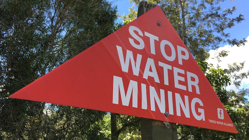 A triangular, red sign reading, Stop Water Mining, nailed to a post in the Tweed Valley